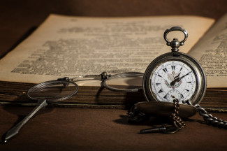 Eine antike Uhr vor einem aufgeschlagenen Buch